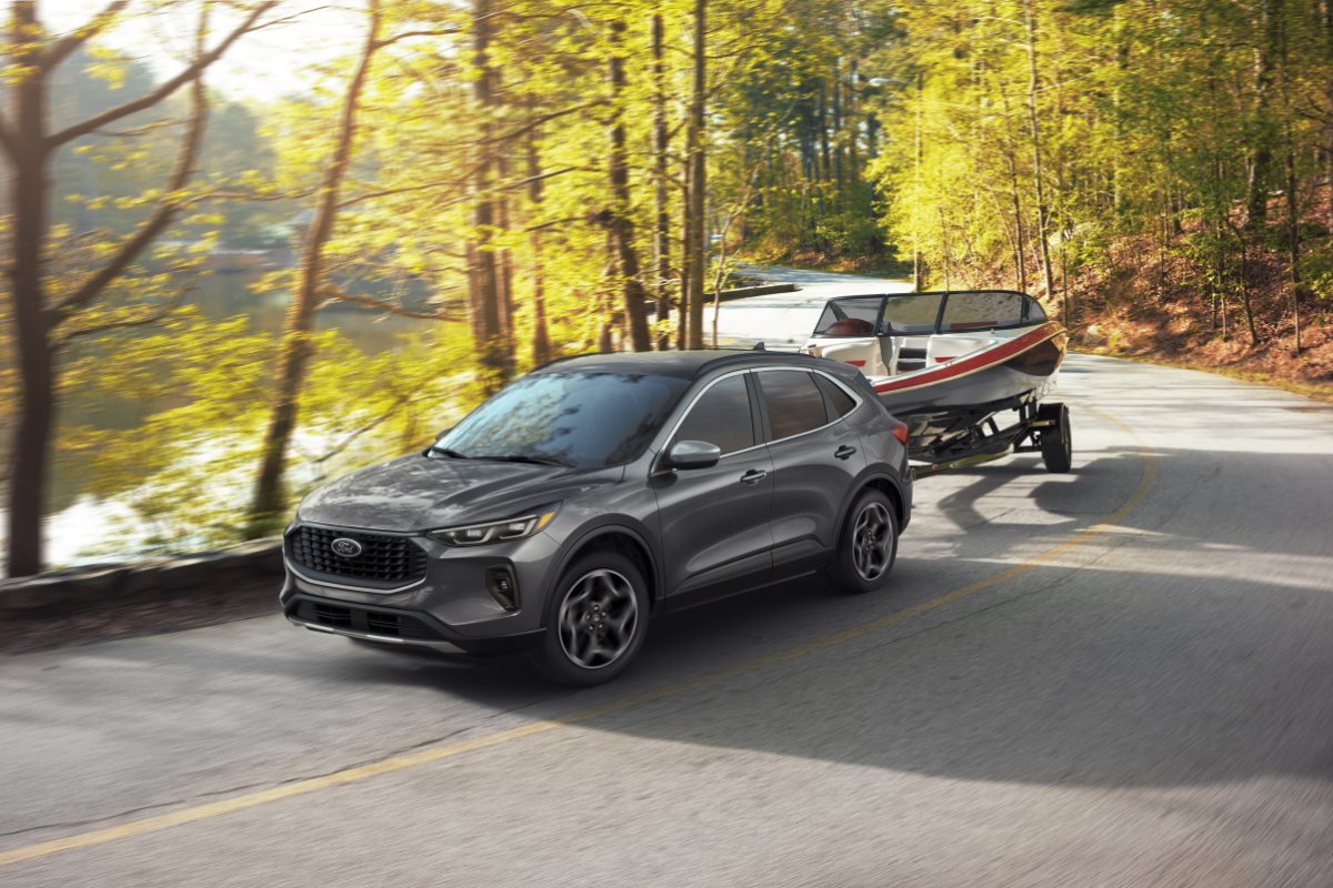 Gray Ford Escape SUV towing a boat along a winding forest road during summer, showcasing the vehicle’s versatility and capability for road trips, outdoor travel, and weekend adventures.