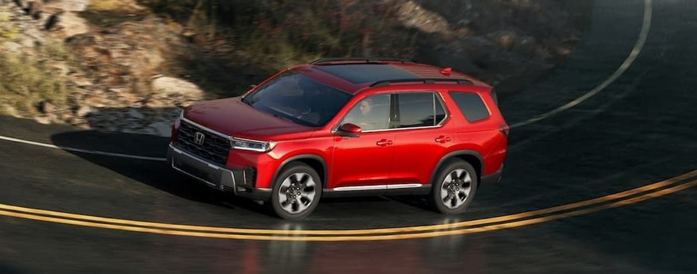 A red 2026 Honda Pilot driving on a highway.