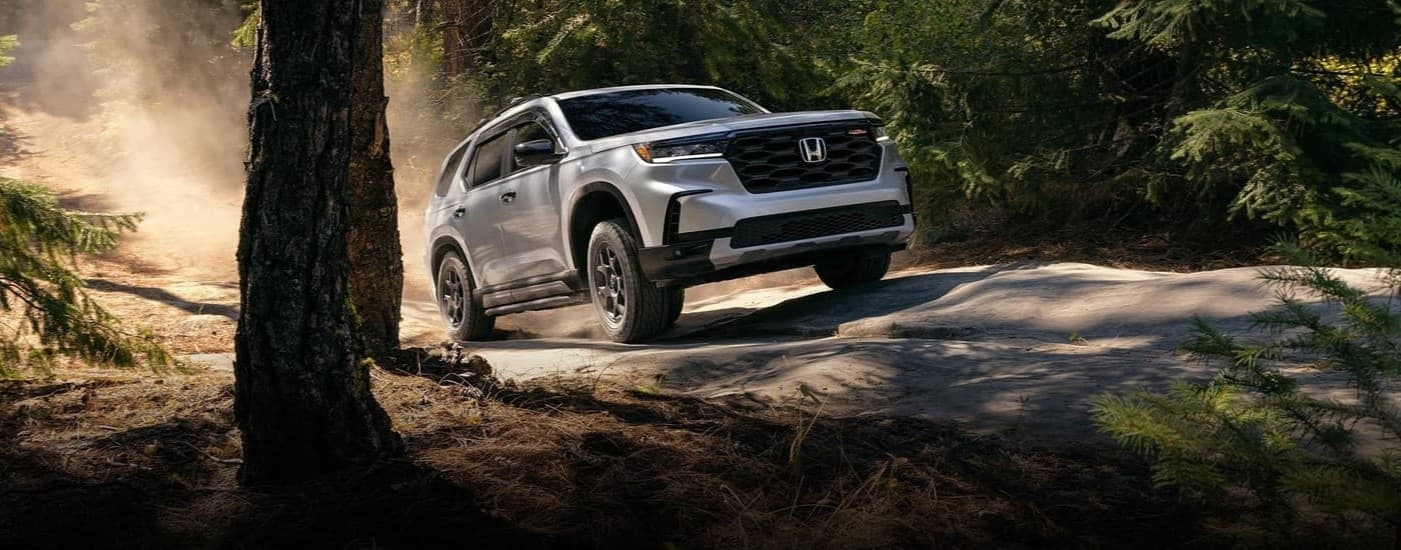 A white 2025 Honda Pilot TrailSport driving offroad.