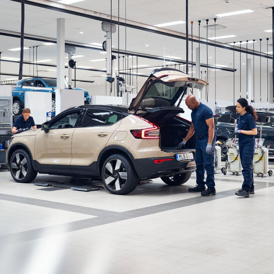 Mechanics in a Volvo workshop inspect an SUV with an open trunk.