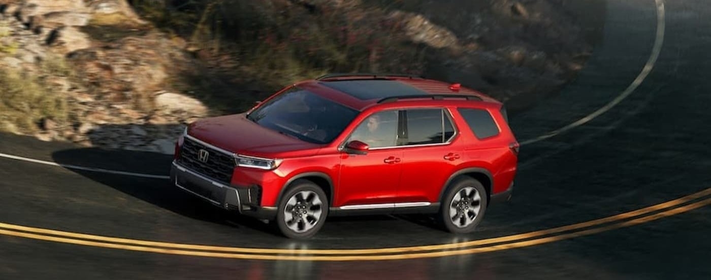 A red 2026 Honda Pilot driving on a highway.