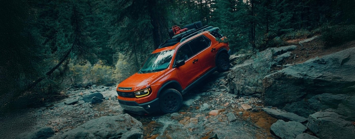 Orange 2026 Honda Passport driving off-road down a hill.