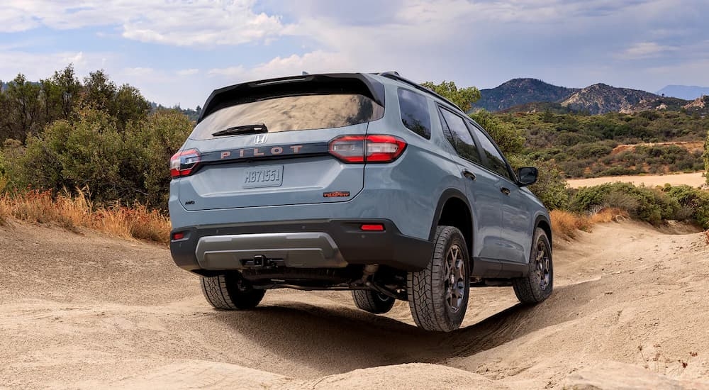 Rear of a blue 2026 Honda Pilot driving off-road.