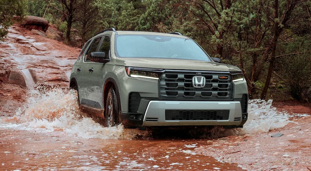 Green 2026 Honda Pilot driving over a shallow river.