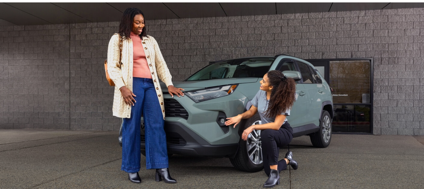Toyota RAV4 XLE shown to a customer outside a modern dealership entrance.