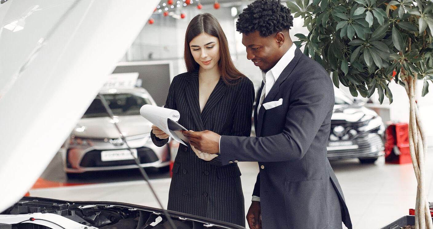 Toyota showroom with a sales consultant and client reviewing paperwork by an open car hood.