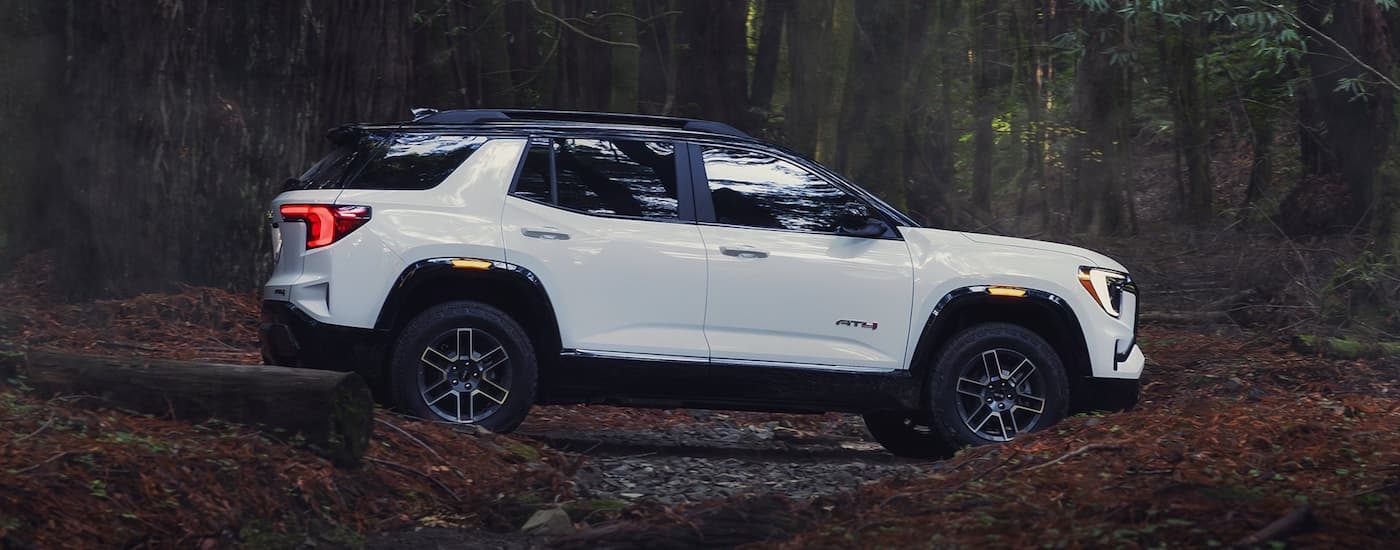 Side of a white 2026 GMC Terrain AT4 driving off-road in a forest.