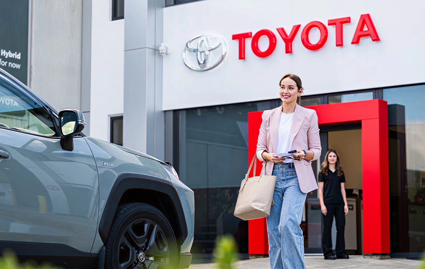 Toyota RAV4 Hybrid parked outside a modern dealership storefront.