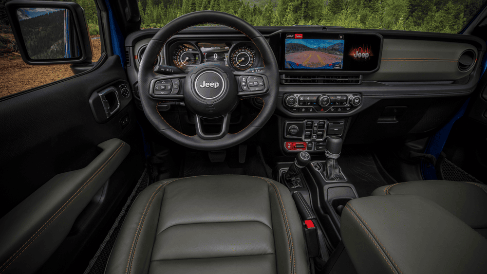 2026 Jeep Gladiator interior in Margate FL with Jeep-branded steering wheel, wide touchscreen infotainment displaying trail camera, dark olive leather seats with orange accent stitching