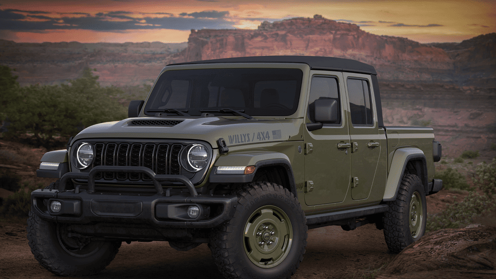 2026 Jeep Gladiator Willys 4x4 in Margate FL in olive green with round LED headlights, black seven-slot grille, off-road tires, and front brush guard against a desert canyon sunset