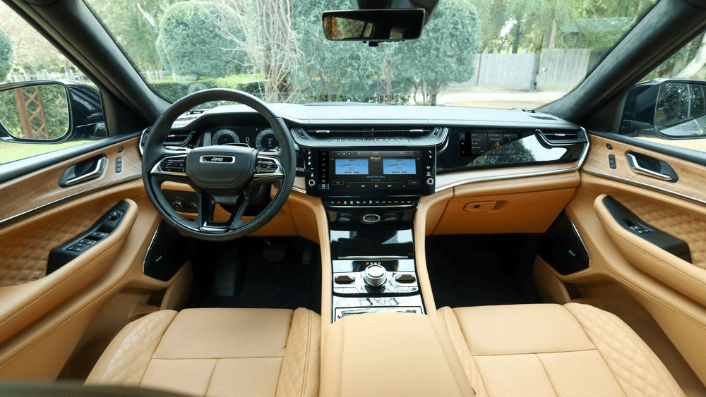2026 Jeep Grand Cherokee L interior in Margate FL featuring Jeep-branded steering wheel, dual McIntosh touchscreen displays, quilted tan leather seats, and wood trim dashboard
