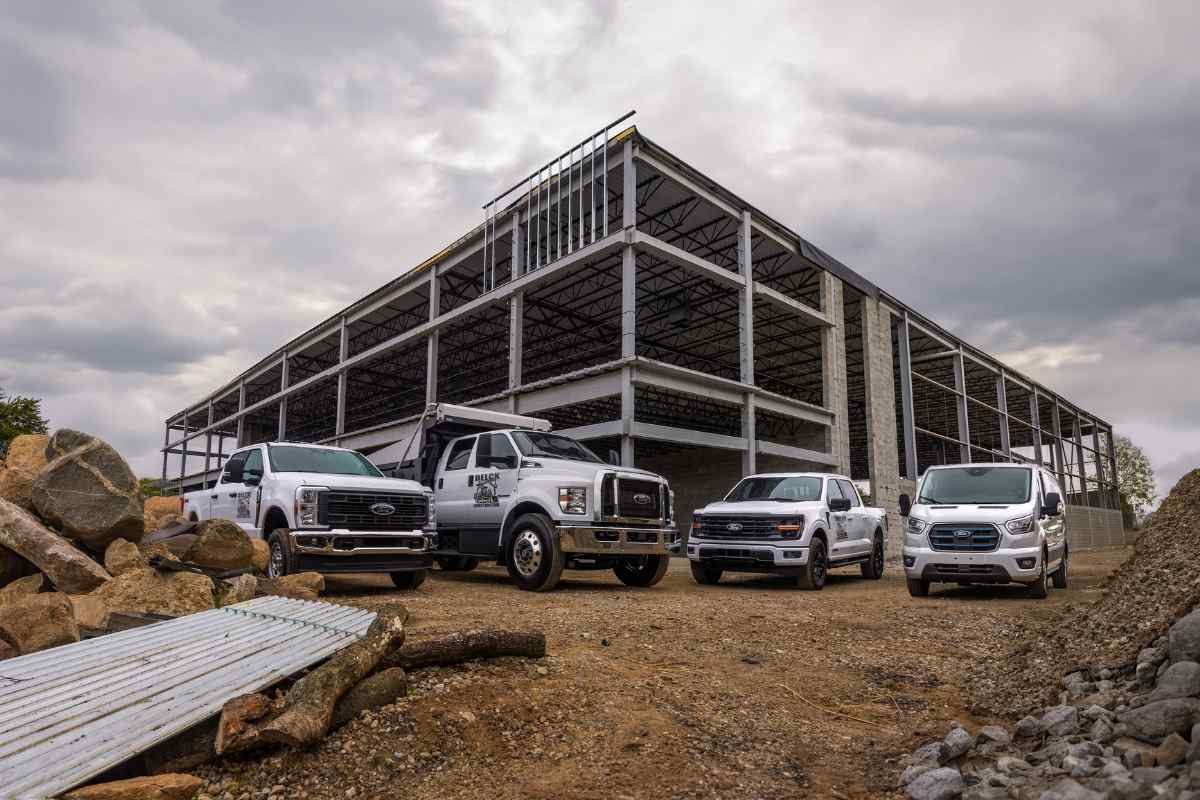 Ford Transit cargo vans and Ford Super Duty work trucks at a commercial construction site with a steel building framework in the background.