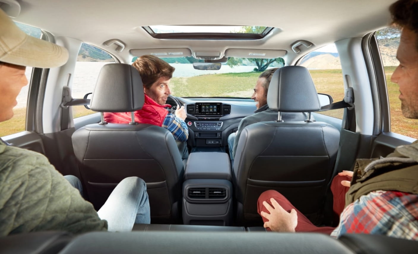 Four people are sitting inside a 2026 Honda Ridgeline parked by a scenic lake.