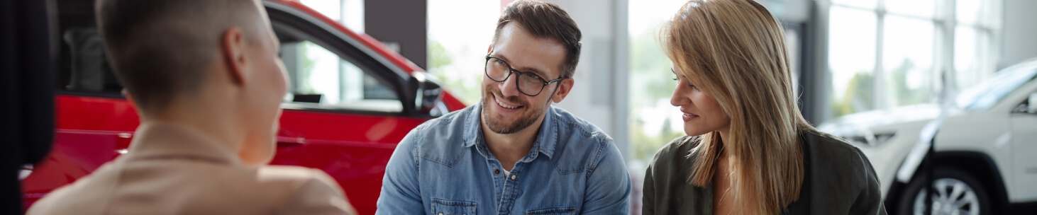 A smiling couple talks to a dealership financing agent.