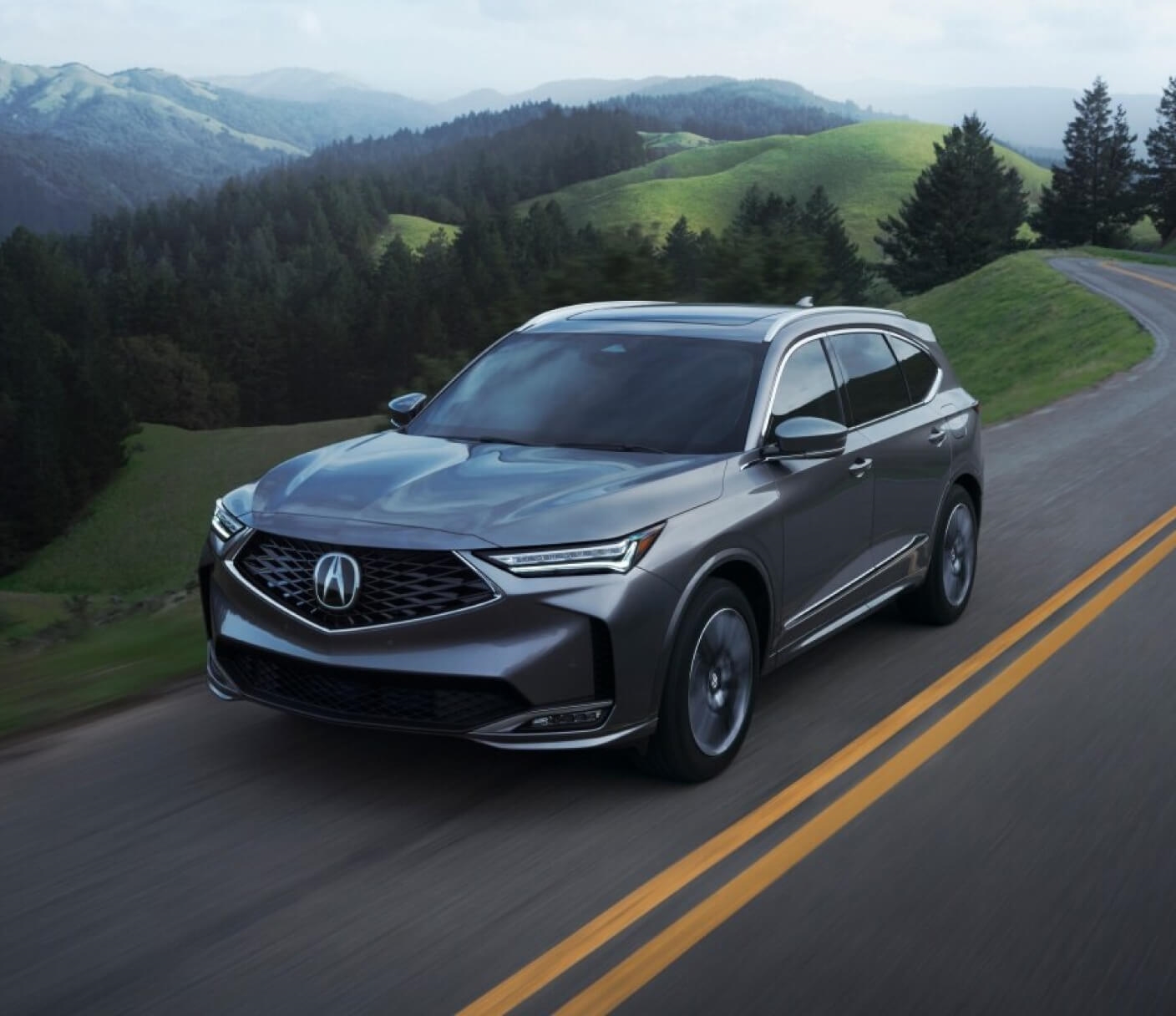 A gray Acura MDX drives down a forest highway.