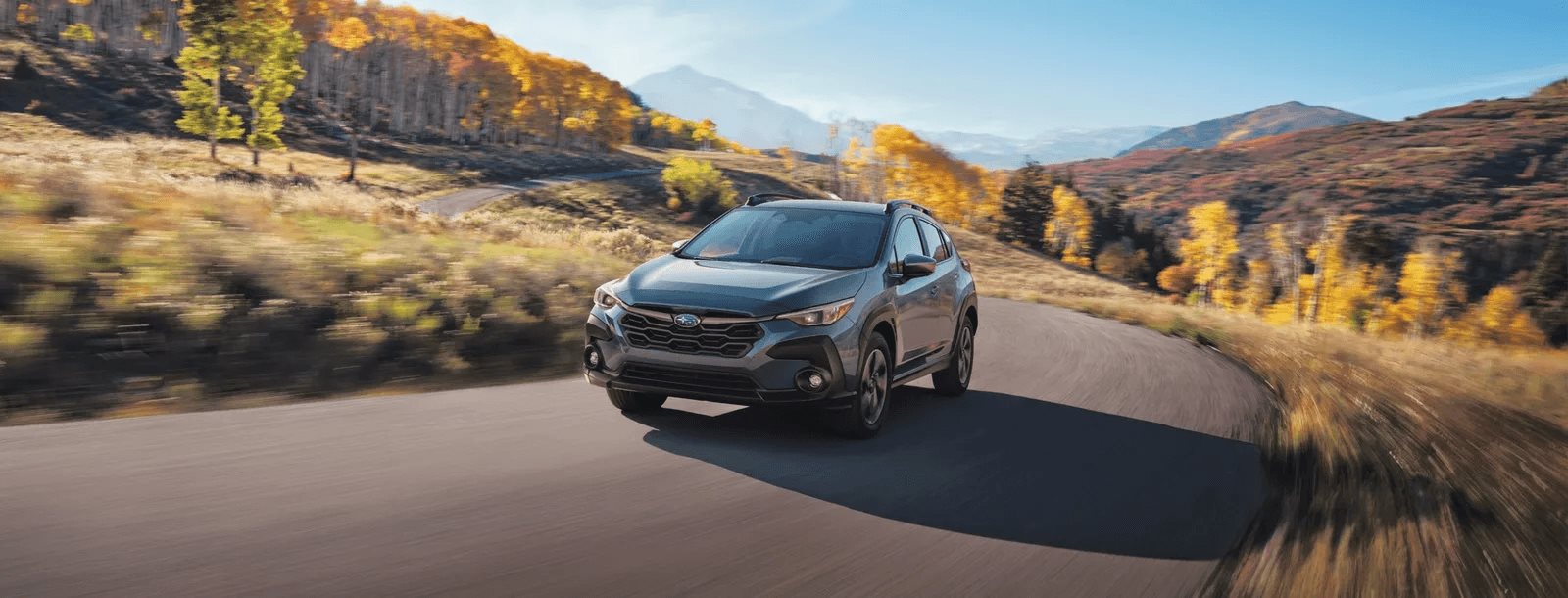 A 2026 Subaru Crosstrek on a winding mountain road through fall foliage and high country, the kind of terrain standard Symmetrical AWD was built for