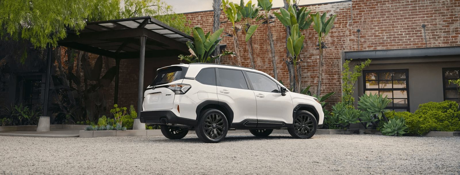 A white Subaru Forester parked in a landscaped brick courtyard, its tall, upright stance and easy ride height visible