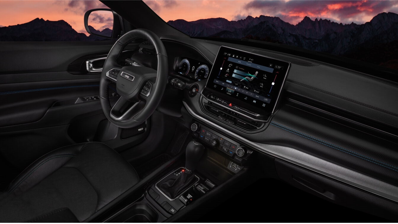 Jeep Compass features a large touchscreen display and ambient dash lighting against a mountain sunset backdrop.