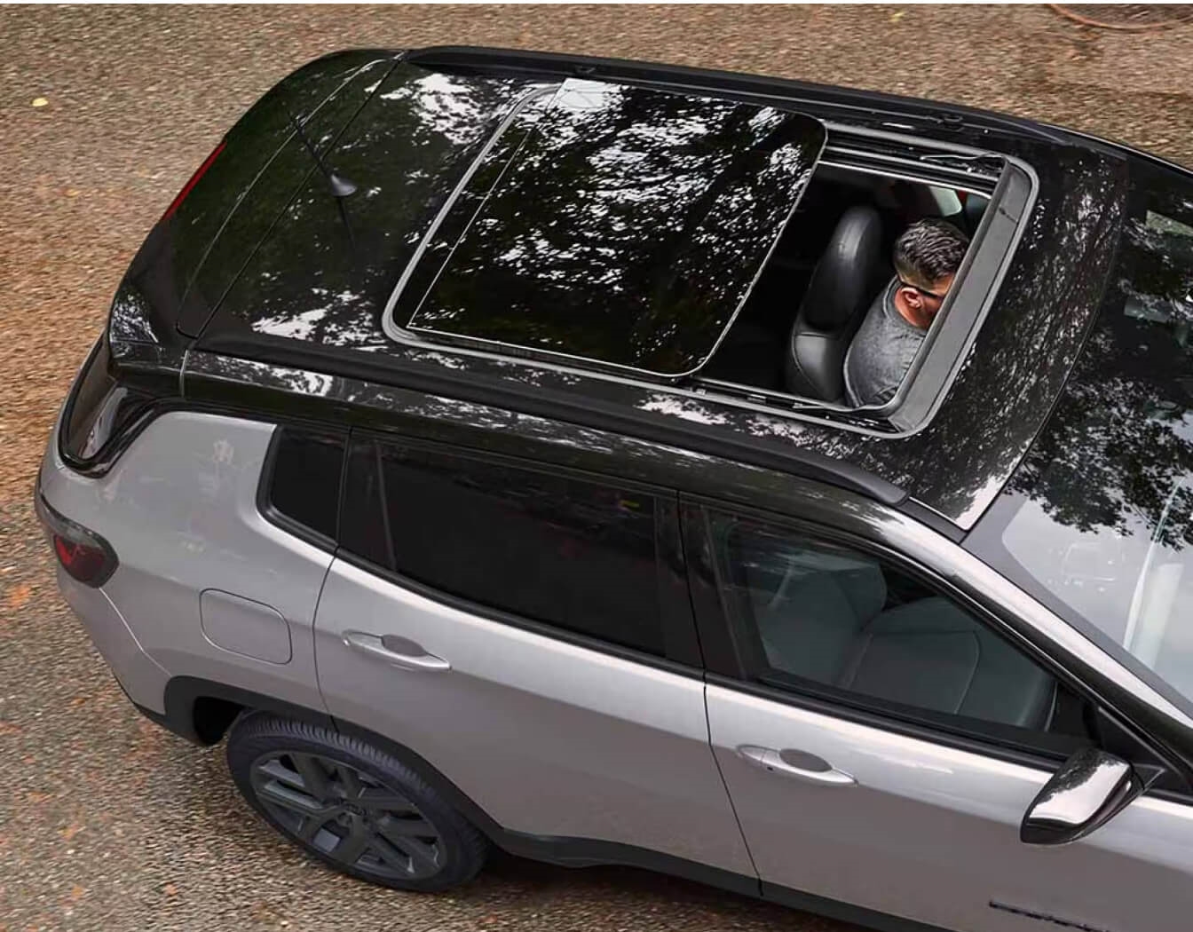 Jeep Compass showcases an open panoramic sunroof from an overhead view on a paved road.