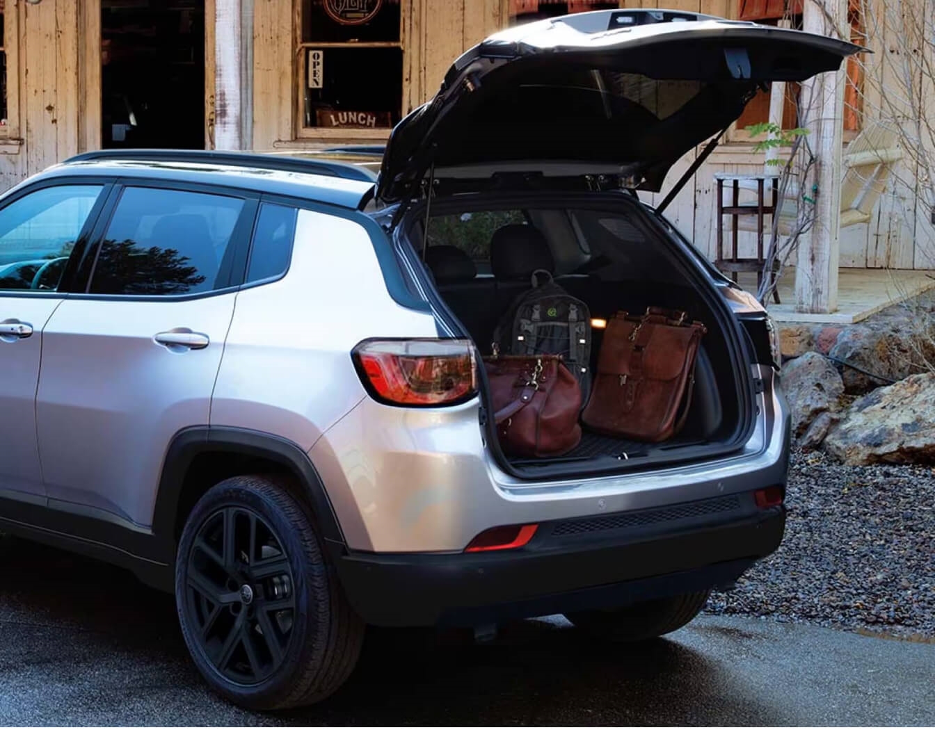 Jeep Compass displays an open liftgate with leather bags in a rustic setting
