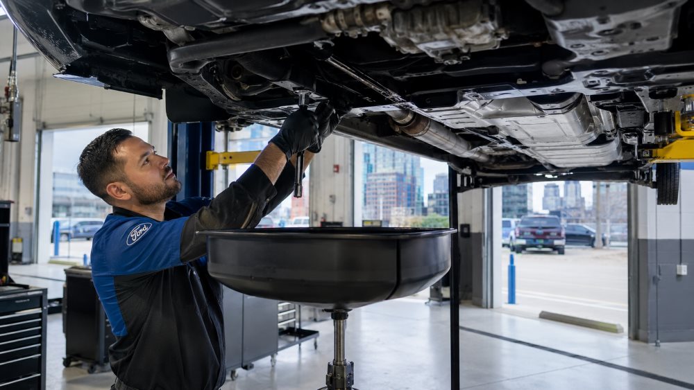 Technician performing a Ford 10-speed transmission fluid service on a lifted vehicle