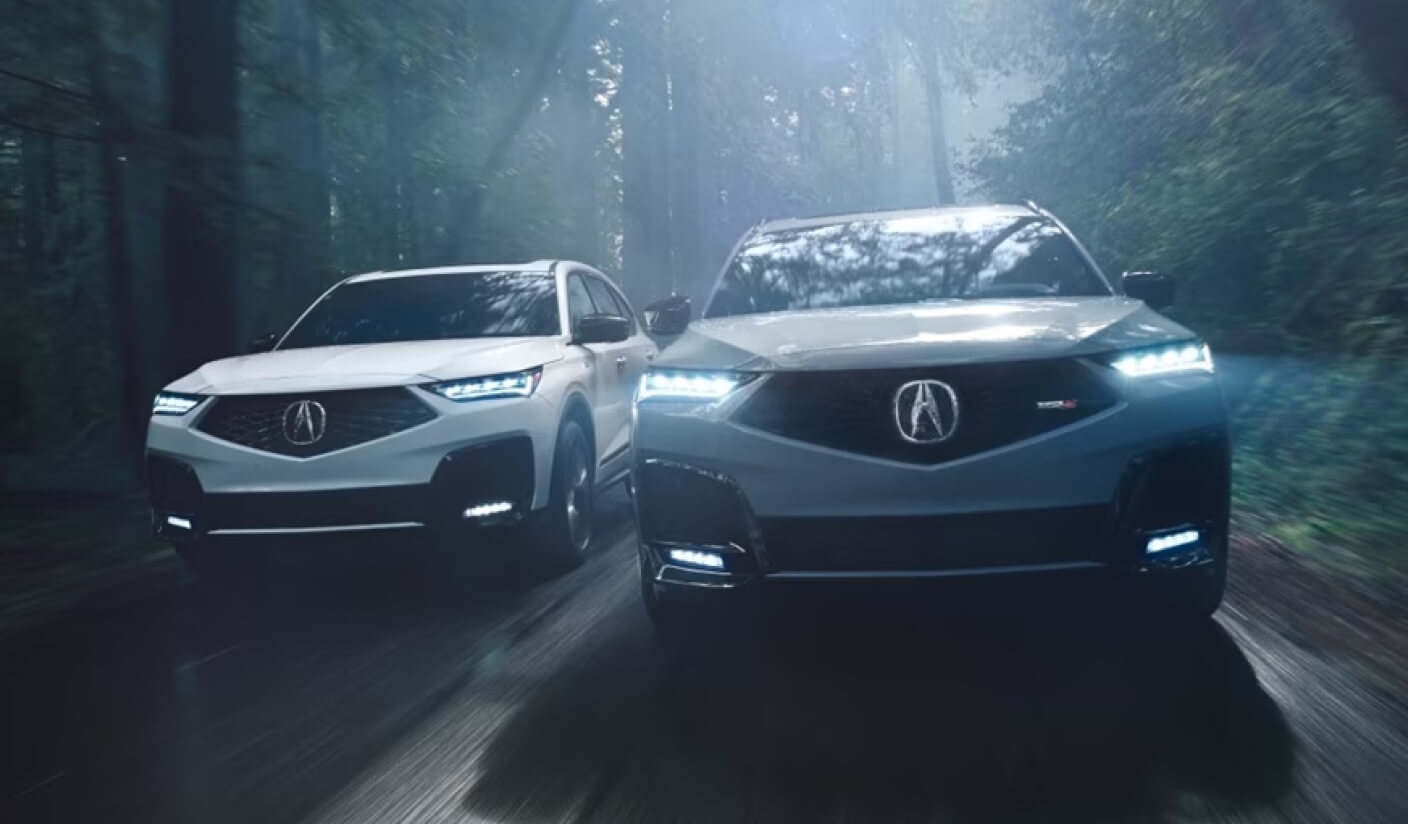 A front view of two Acura MDX models speeding down a forest road.