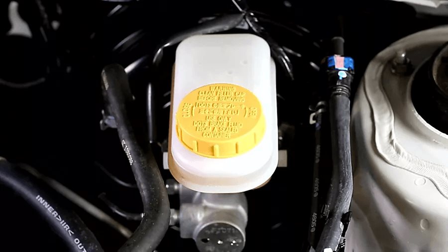 Subaru brake-fluid reservoir under the hood, yellow filler cap stamped with the brake-fluid spec, reading clean filler cap before removing.