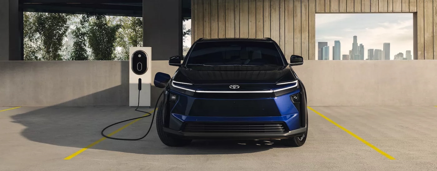 Front of a dark blue 2026 Toyota bZ plugged in at a charging station.