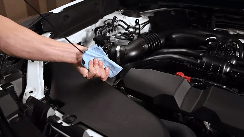 Hand wiping the engine oil dipstick clean with a cloth in a Subaru engine bay.