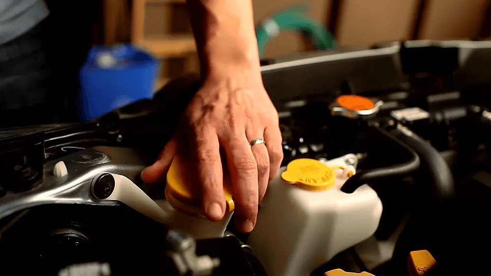 Hand on the yellow engine oil filler cap on a Subaru boxer engine.