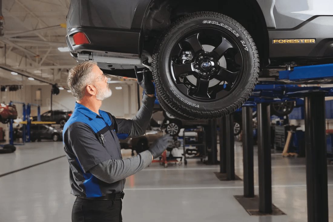 A Subaru Certified technician inspecting a lifted Forester from underneath in the Findlay Subaru Prescott service bay.