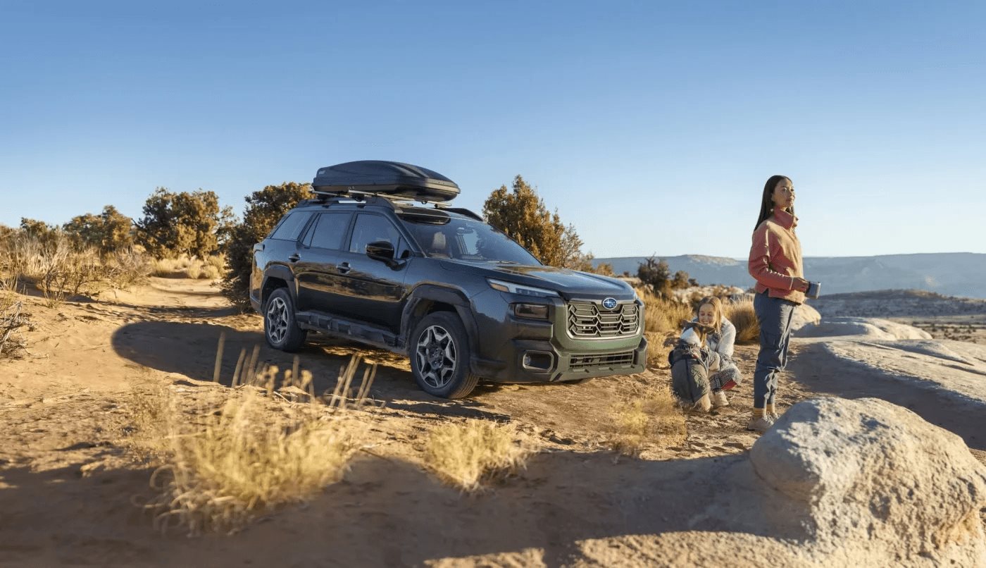 A family beside a green Subaru Outback Wilderness parked on a high-desert overlook at golden hour.