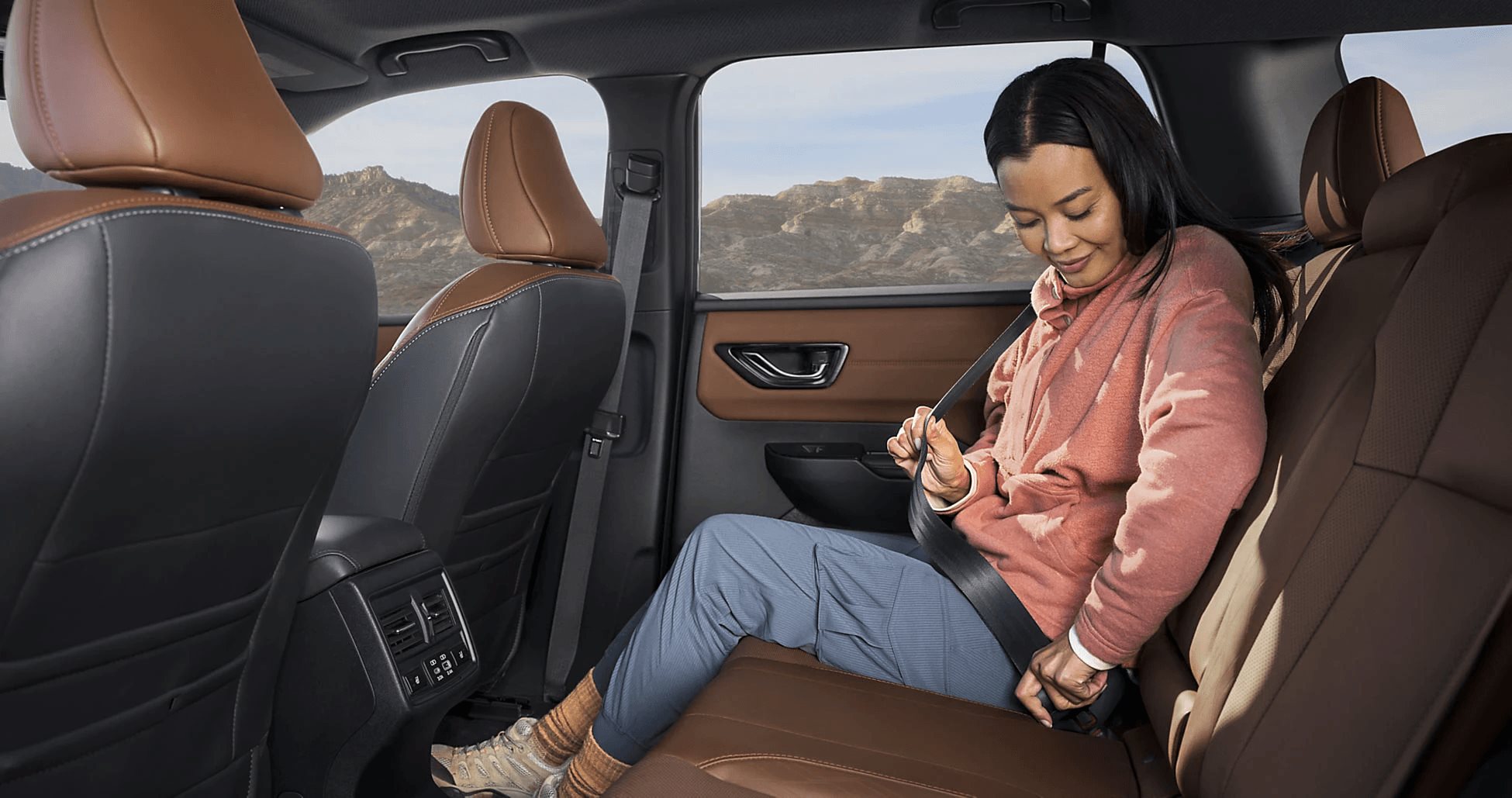 A passenger buckling into the spacious rear seat of a Subaru Outback, mountains visible outside.