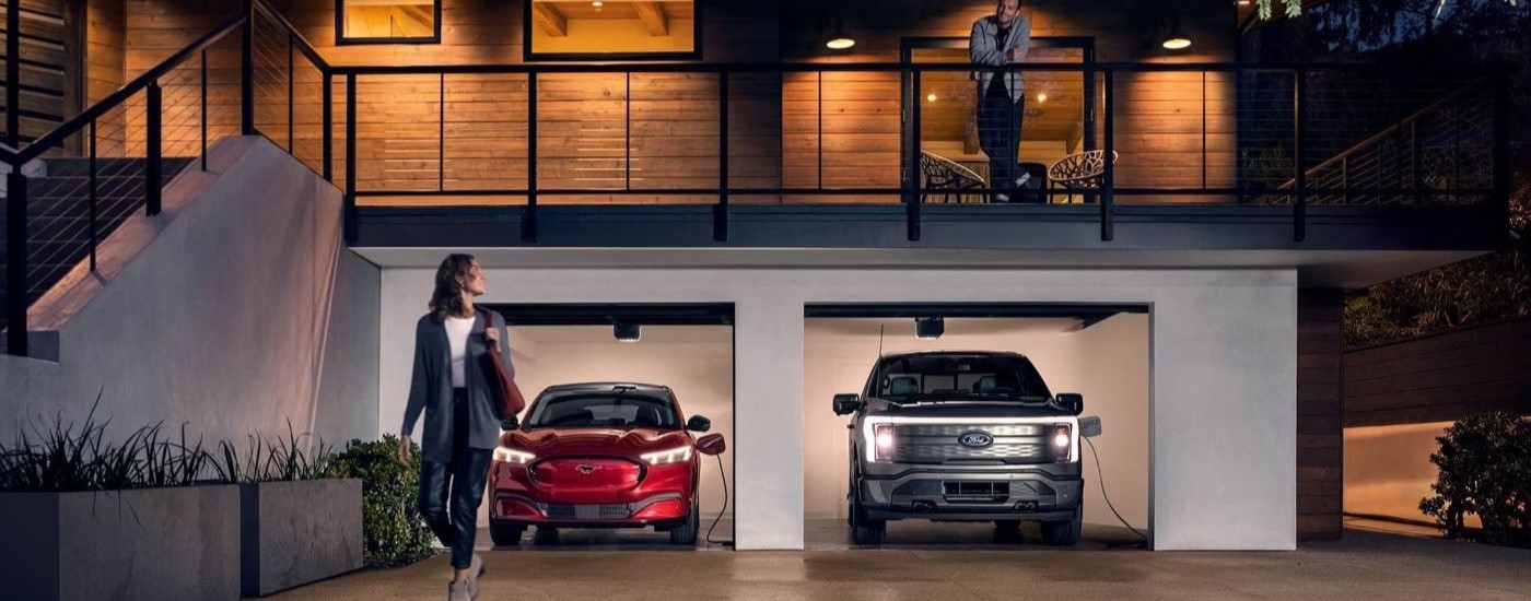 Red 2023 Ford Mustang Mach-E and a black F-150 Lightning are  charging in a garage