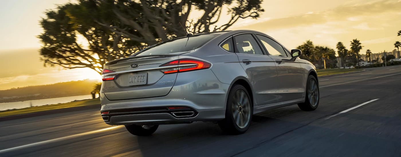 silver 2017 Ford Fusion Platinum is shown from the rear driving past a lake