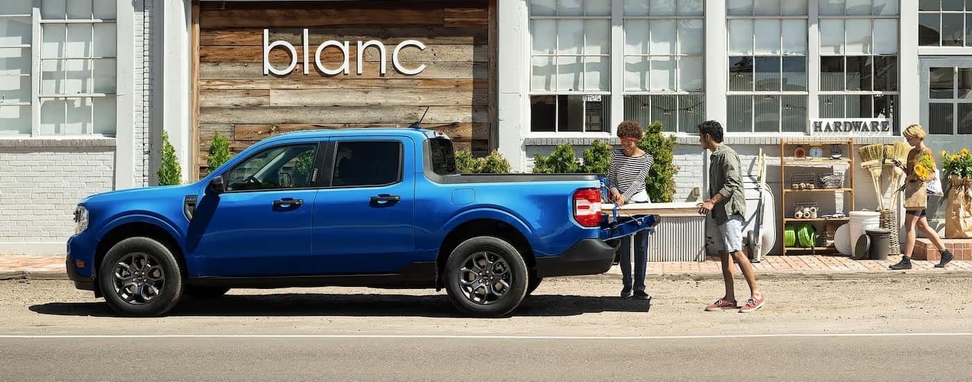 A blue 2025 Ford Maverick is shown parked near a hardware store.