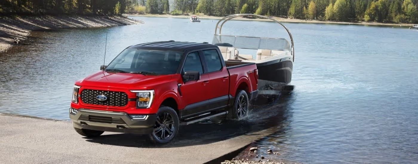 A red 2023 Ford F-150 Heritage Edition is shown towing a boat out of water.
