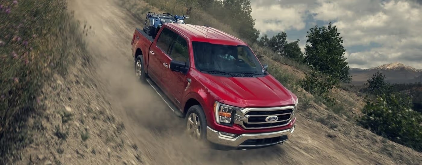 A red 2023 Ford F-150 is shown descending a dusty trail.