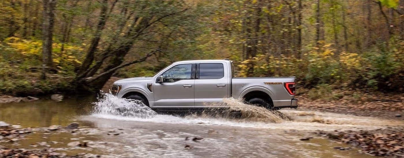 A silver 2021 Ford F-150 Tremor is shown from the side while driving through a creek.