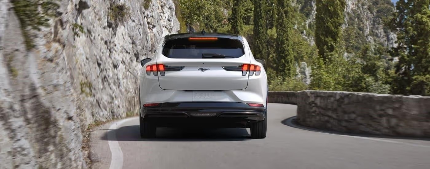 A white 2023 Ford Mustang Mach-E is shown from the rear on a winding road.