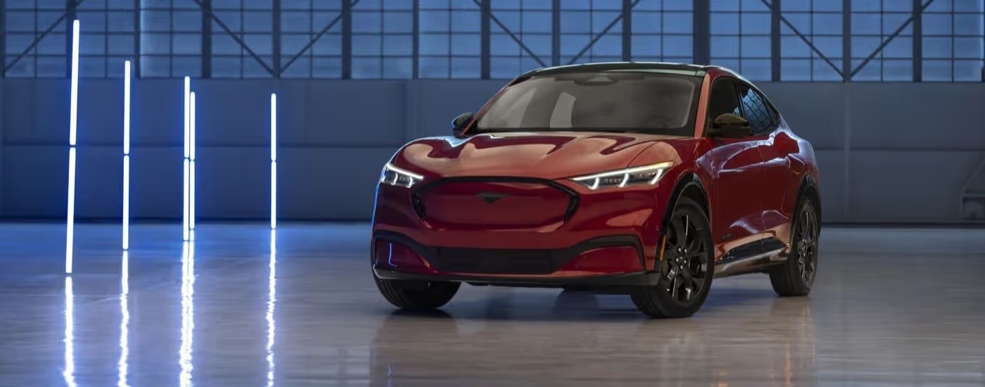A red 2023 Ford Mustang Mach-E for sale is shown parked in a warehouse.
