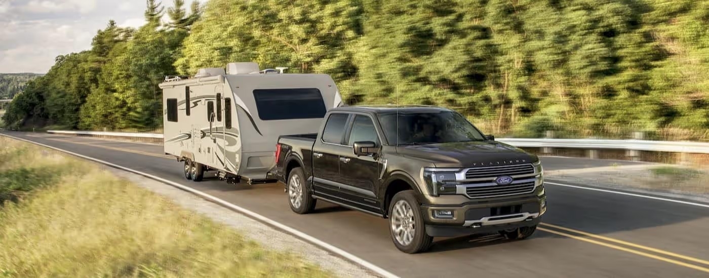 A black 2025 Ford F-150 Platinum Plus is shown towing a trailer.