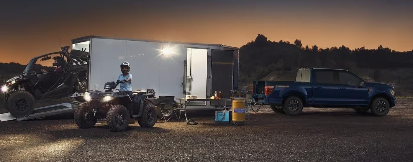 A blue 2025 Ford F-150 Tremor is shown parked off-road while towing a trailer.