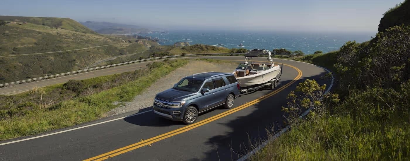 A grey 2023 Ford Expedition Platinum is shown towing a boat after leaving a Ford service center near Marietta.