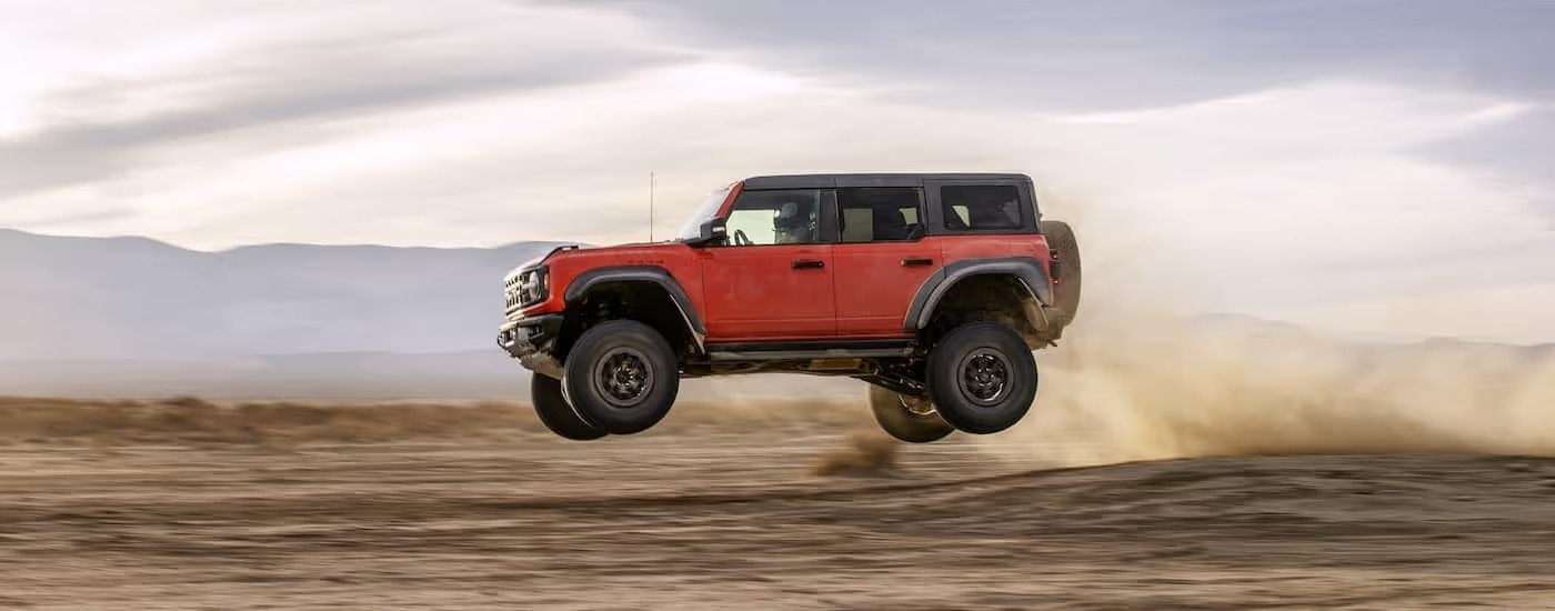 An orange 2024 Ford Bronco Raptor is shown from the side while jumping.