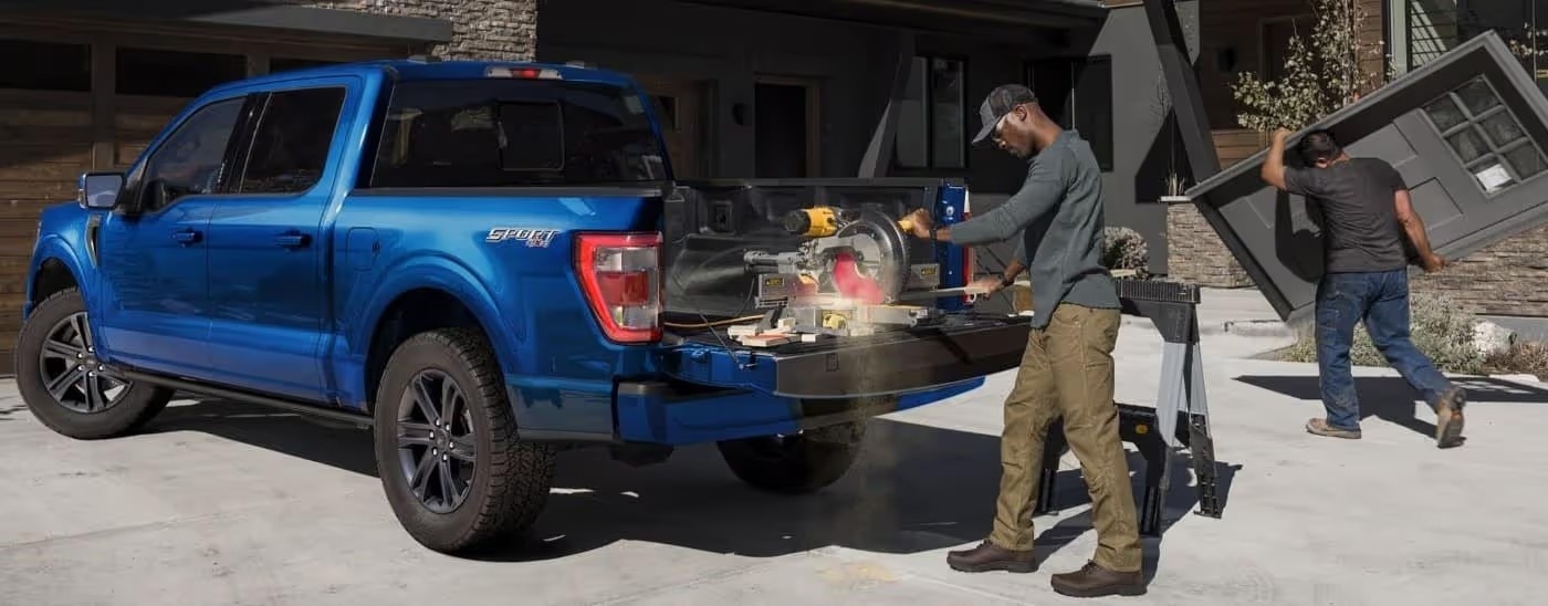 A man using a saw in the bed of a blue 2024 Ford F-150 Sport.