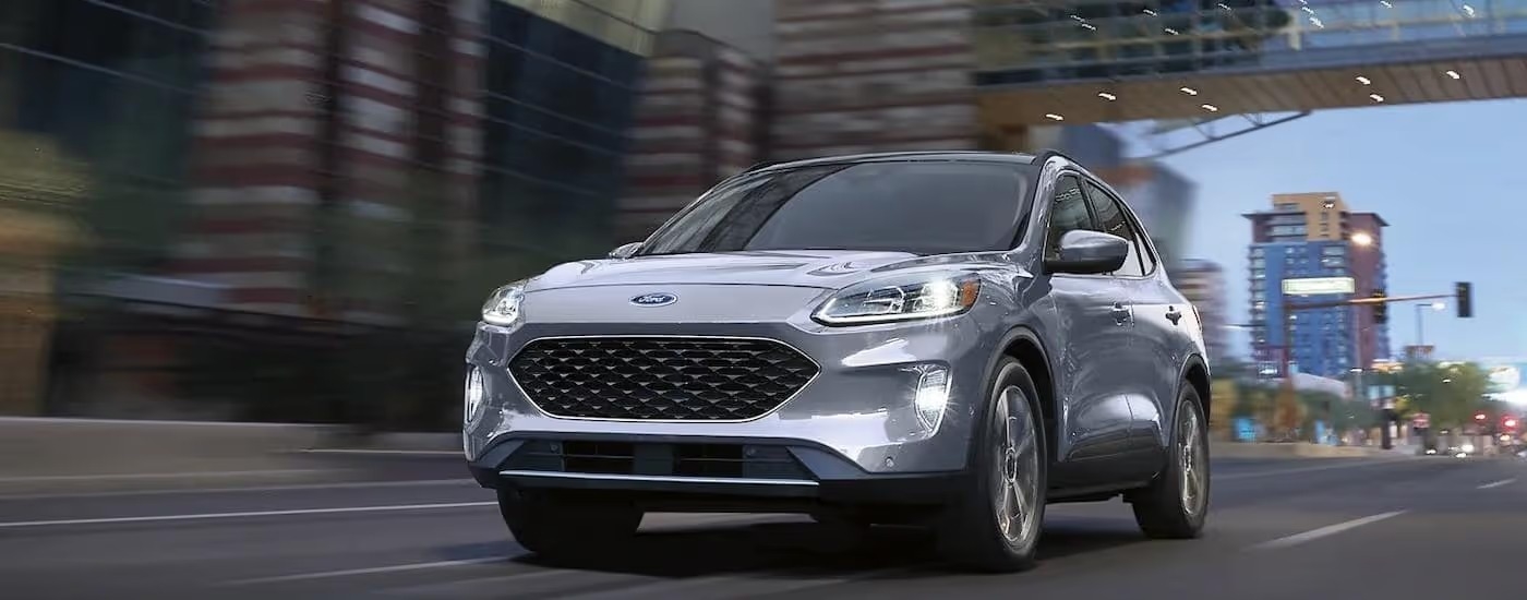A silver 2022 Ford Escape Titanium Hybrid is driving on a city highway.
