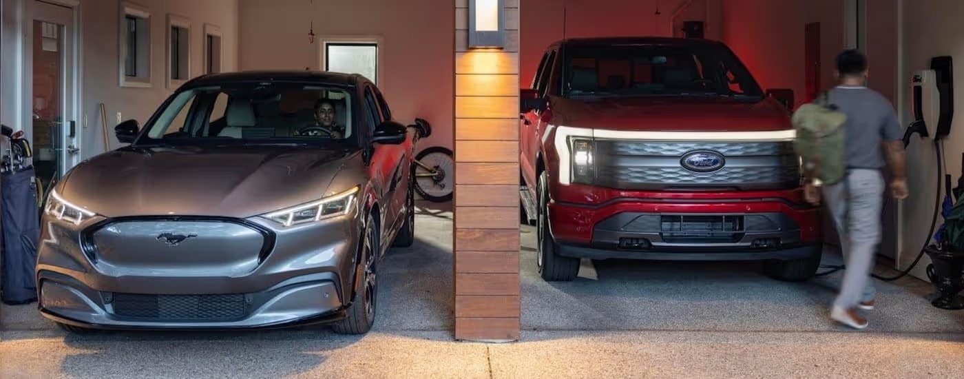 A grey 2024 Ford Mustang Mach-E and a red 2023 Ford Lightning are parked in a garage.