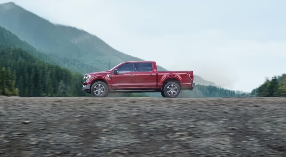 A red 2023 Ford F-150 FX4 is shown from the side driving on a trail.