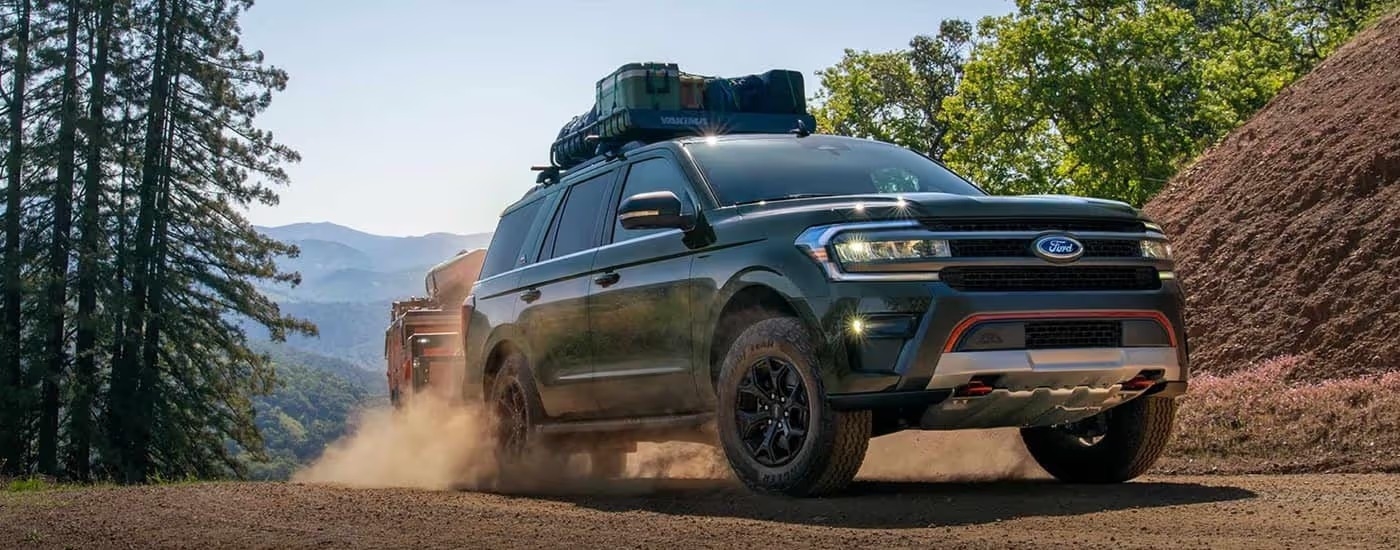 A green 2024 Ford Expedition Timberline towing a trailer while driving on a dirt path.